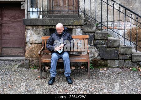 Anziano uomo anziano seduto su panca e regola la maschera viso, St. Nicholas e San Maria Cimitero i, Prenzlauer Allee 1. Berlino Foto Stock