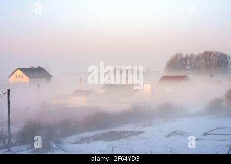 Russia, regione di Kaliningrad, 22 febbraio 2021. Tetti di case di villaggio. Nebbia sopra le case del villaggio. Fumo dal camino. Foto Stock