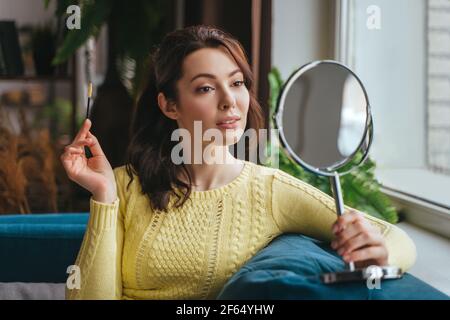 Giovane bella donna fa trucco a casa mentre si guarda in lo specchio Foto Stock