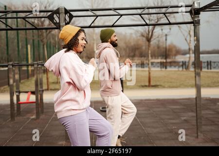 vista laterale di una coppia afroamericana sorridente che corre sul posto all'aperto, sfondo sfocato Foto Stock