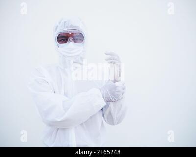 Ritratto di giovane medico o scienziato asiatico in uniforme DPI suite tenendo le mani mentre si guarda avanti. Coronavirus o COVID-19 concetto isolato bianco Foto Stock