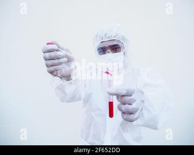 Medico o scienziato asiatico in uniforme DPI suite. Indumenti protettivi individuali per far cadere il sangue nella provetta per gli esami del sangue. Coronavirus o COVID-19 conc Foto Stock