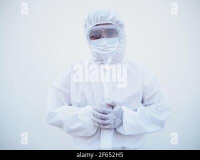 Ritratto di giovane medico o scienziato asiatico in uniforme DPI suite tenendo le mani mentre si guarda avanti. Coronavirus o COVID-19 concetto isolato bianco Foto Stock