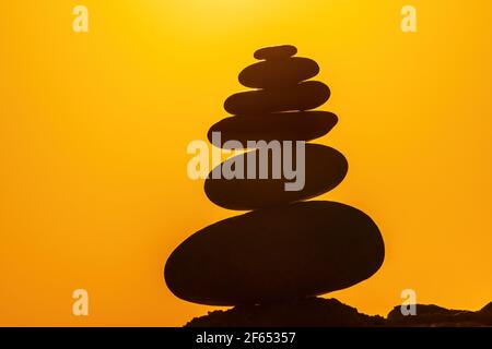 Profilo a piramide di ciottoli bilanciato sulla spiaggia. Astratto caldo tramonto bokeh con Mare sullo sfondo. Pietre Zen sulla spiaggia di mare, meditazione, spa Foto Stock