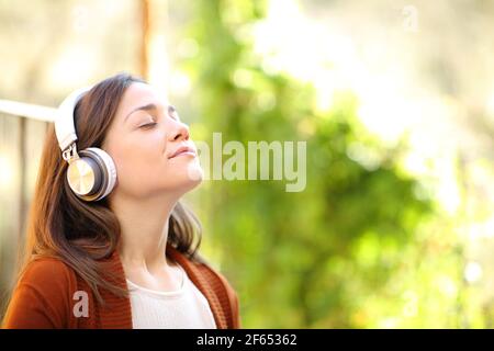 Donna rilassata che indossa cuffie che respirano aria fresca meditando l'ascolto musica in un giardino della casa Foto Stock