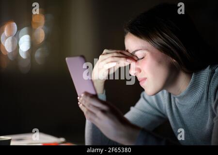 Donna stanca che soffre di affaticamento degli occhi utilizzando il telefono cellulare di notte a casa Foto Stock
