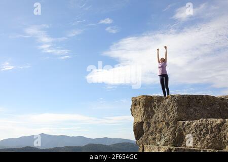 Runner eccitato che alza le braccia celebrando il successo nella parte superiore di una scogliera Foto Stock