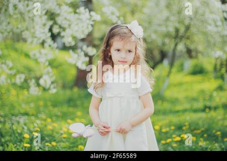 Bambina in bianco tenere uova giocattolo di pasqua su bastoni nel giardino delle ciliegie primaverili Foto Stock