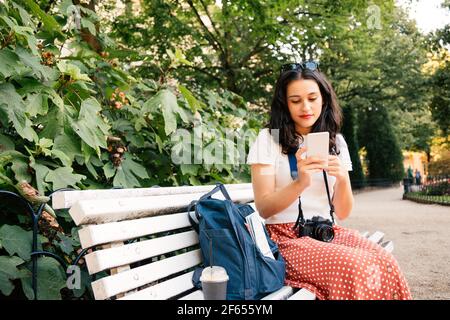 Bella donna turistica che usa il suo smartphone seduto in una città il parco è Foto Stock