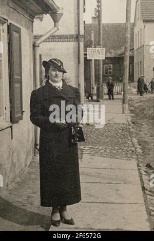 Germania - CIRCA 1930: Donna indossando cappotto e ritratto cappello. Donna in piedi sulla strada. Donna all'aperto. Vintage carte de Viste Art Deco foto epoca Foto Stock