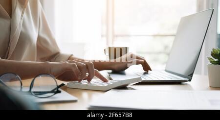 Primo piano mano di donna che usa il computer calcolando le finanze o le tasse della famiglia sulla macchina, femmina gestire le spese della famiglia domestica, utilizzando la calcolatrice Foto Stock