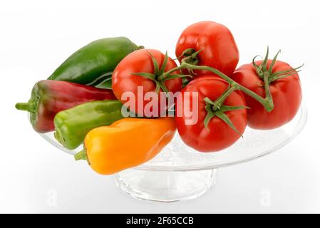 pomodori e peperoni su piatto rialzato in vetro trasparente - verdure rosse, gialle e verdi isolate su sfondo bianco Foto Stock