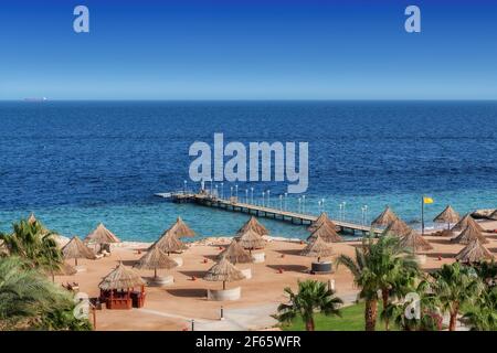 Spiaggia soleggiata in resort tropicale con palme e ombrelloni In Mar Rosso Foto Stock