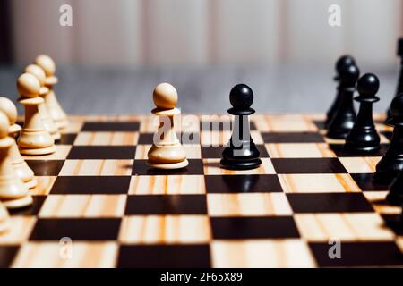 Primo piano di due pedine sulla scacchiera su un tavolo con pezzi bianchi e neri. Concetto di gioco di scacchi, concorso di scacchi Foto Stock