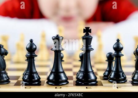Primo piano di alcuni pezzi scacchi neri con il volto di una ragazza fuori fuoco sullo sfondo. Concetto di giocare a scacchi a casa, hobby a casa Foto Stock