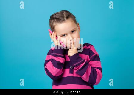 primo piano ritratto di una ragazza seria con pigtail che fa la telefonata, tenendo il dito alla bocca, segreto o richiesta di silenzio, isolato su sfondo blu Foto Stock