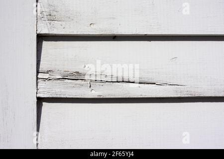 Vecchio pannello laterale verniciato bianco accanto a un pannello di rivestimento che mostra crepe e usura alla luce del mattino. Foto Stock