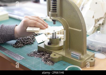 primo piano le mani dell'uomo inseriscono gli anelli di tenuta e gli occhielli nelle etichette degli abiti su una grande pressa manuale professionale gommino Foto Stock