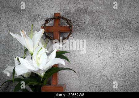 Croce con gigli bianchi e corona di spine su sfondo grigio. Concetto di Pasqua del cristianesimo. Foto Stock