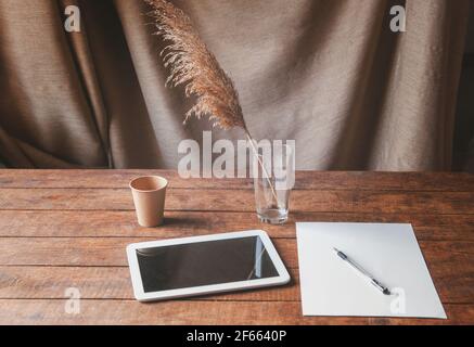 Ambiente di lavoro moderno con tablet pc sul tavolo. Sul tavolo è un computer tablet con un foglio di carta bianca, fiori secchi in un bicchiere e un dis Foto Stock