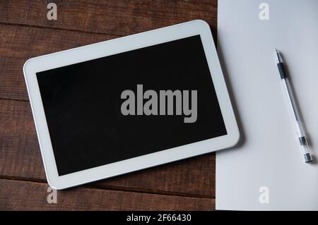 Ambiente di lavoro moderno con tablet pc sul tavolo. Sul tavolo è un computer tablet con un foglio di carta bianca, fiori secchi in un bicchiere e un dis Foto Stock