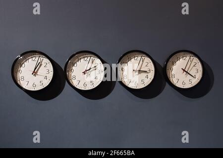 Quattro orologi sulla parete nera Foto Stock