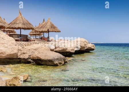 Spiaggia tropicale soleggiata con ombrelloni nella spiaggia di corallo del Mar Rosso, Egitto, Africa. Foto Stock