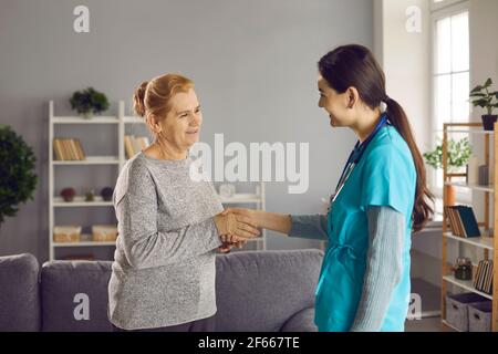Paziente anziano felice che si familiarizza con un'infermiera giovane amichevole o medico Foto Stock