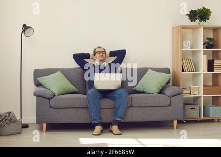 Uomo maturo calmo con gli occhi chiusi rilassandosi su un comodo divano con computer portatile Foto Stock