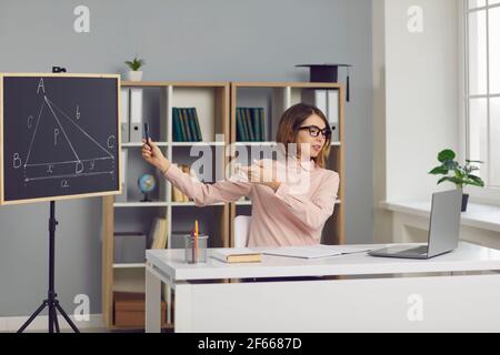 L'insegnante di matematica si siede in classe e spiega un nuovo argomento della lezione online con un laptop. Foto Stock