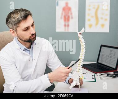 Trattamento dell'ernia intervertebrale. Fisioterapista maturo che utilizza il modello anatomico della colonna vertebrale per analizzare le aree problematiche della colonna vertebrale umana Foto Stock