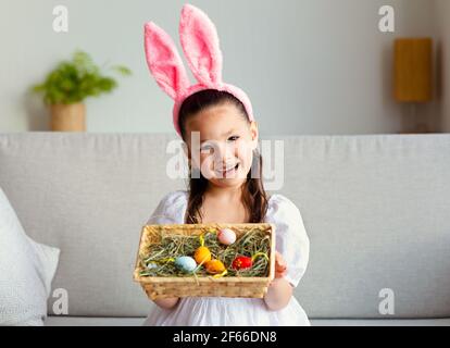 Ragazza vestita come coniglio di Pasqua mostrando cesto con uova al coperto Foto Stock