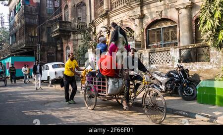 Kolkata, Bengala Occidentale, India - Gennaio 2018: Un rickshaw ciclistico con un idolo di una Dea che passa davanti a un vecchio edificio d'epoca nella zona di Kumartuli del Th Foto Stock