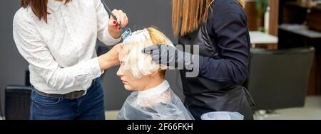 Due donne parrucchieri tintura capelli di giovane donna caucasica in salone di parrucchiere Foto Stock