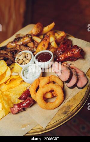 Carne su tavola di legno. Ali di pollo fritte, costolette di maiale, verdure alla griglia, patatine fritte. Antipasto di birra con salse. Immagine di sfondo Foto Stock