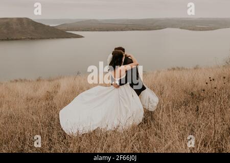 Una coppia amorevole sposi sposi novelli in un vestito bianco e. un vestito camminare abbraccio baciarsi sull'erba alta dentro il campo estivo d'autunno sulla montagna sopra il Foto Stock