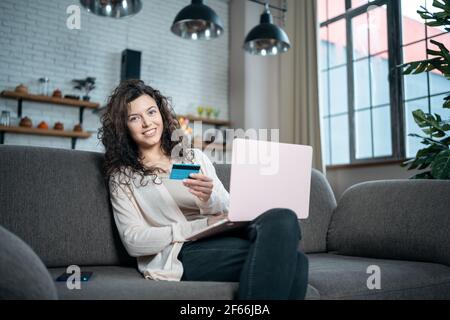 giovane donna effettua l'acquisto online con carta di credito e computer portatile sul divano a casa Foto Stock