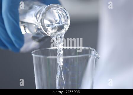 Chimico scienziato in guanti versare l'acqua dal pallone in vetro primo piano Foto Stock