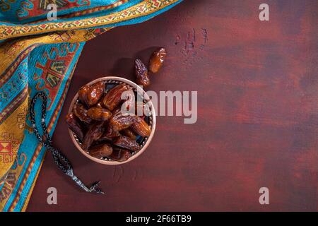 Piatto di bronzo con datteri e tasbih (misbaha) su vecchio tavolo di legno rosso-marrone. Ramadan sfondo. Disposizione piatta. Messa a fuoco selettiva. Foto Stock