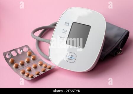 Monitor automatico della pressione sanguigna e blister con pillole su sfondo rosa. Tonometro elettronico per uso medico. Concetto di assistenza sanitaria Foto Stock