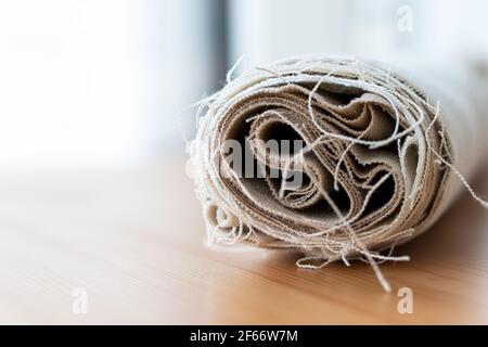 Rotolo di tessuto di lino naturale con fili sporgenti su un tavolo di legno. Messa a fuoco selettiva. Vista in primo piano. Sfondo sfocato Foto Stock