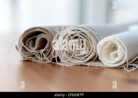 Tre rotoli di tessuto di lino naturale in diversi colori con fili sporgenti su un tavolo di legno. Messa a fuoco selettiva. Vista in primo piano. Sfondo sfocato Foto Stock