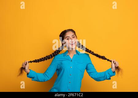 Felice donna indiana che tiene e tirando le sue due lunghe trecce Foto Stock