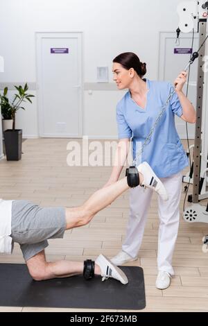 fisioterapista sorridente che sostiene la gamba dell'uomo che lavora in riabilitazione centro Foto Stock