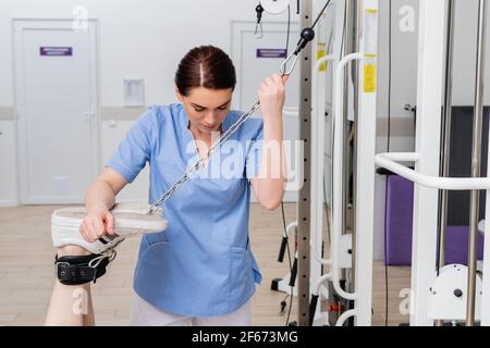 riabilitologo che sostiene le gambe dell'uomo che lavora sulla macchina di esercitazione Foto Stock