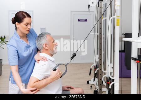 fisioterapista di brunette che sostiene l'uomo maturo che si esercita nel centro di riabilitazione Foto Stock