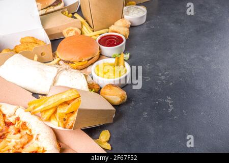 Consegna fastfood ordinare online concetto di cibo. Ampia scelta di piatti assortiti da asporto pizza, patatine fritte, bocconcini di pollo fritti, hamburger, insalate, chic Foto Stock