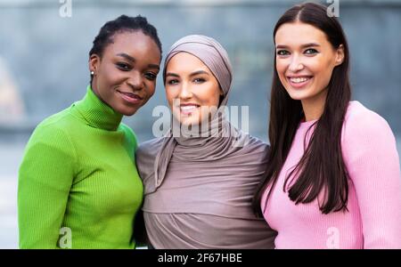 Donne afroamericane, musulmane e caucasiche che posano insieme in piedi fuori Foto Stock