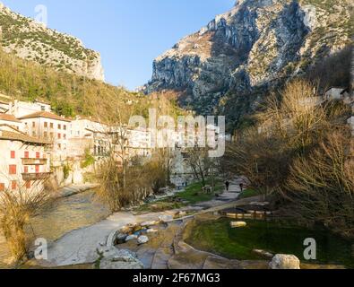 Edifici in villaggio sotto ripide pareti di roccia calcarea dei monti Vercors, Francia. Sole del mattino. Foto Stock