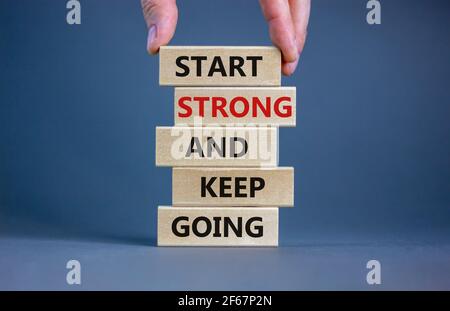 Inizia forte e continua a andare simbolo. Le parole di concetto "Start strong and Keep Going" su blocchi di legno su uno splendido sfondo grigio. Mano uomo d'affari. Autobus Foto Stock